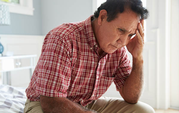 A distressed man sitting on a bed with his head in his hands